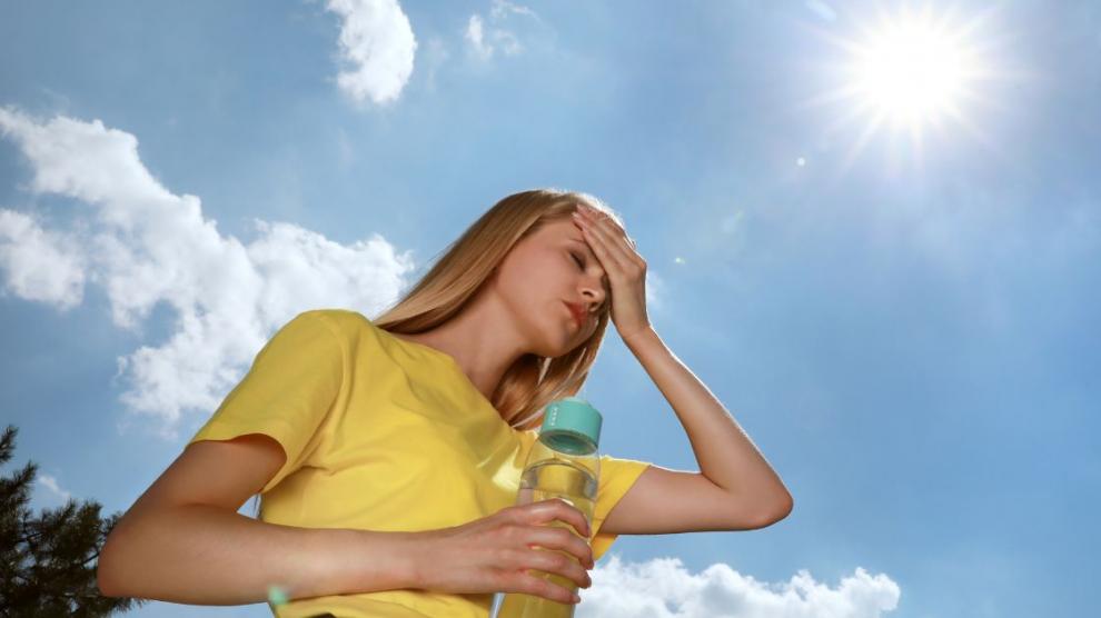 Mujer sintiéndose deshidratada por las altas temperaturas y sujetando una botella de agua
